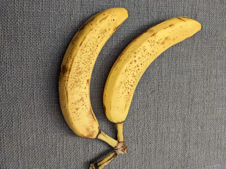 Two ripe, speckled bananas on grey linen, seen from above