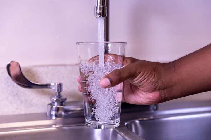 A hand filling a glass with water from a kitchen tap