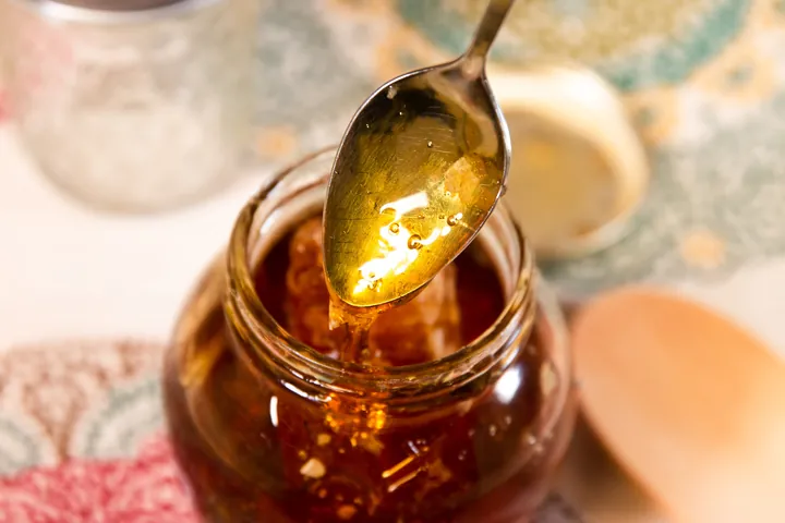 A spoon lifting golden honey from a small jar with honeycomb inside