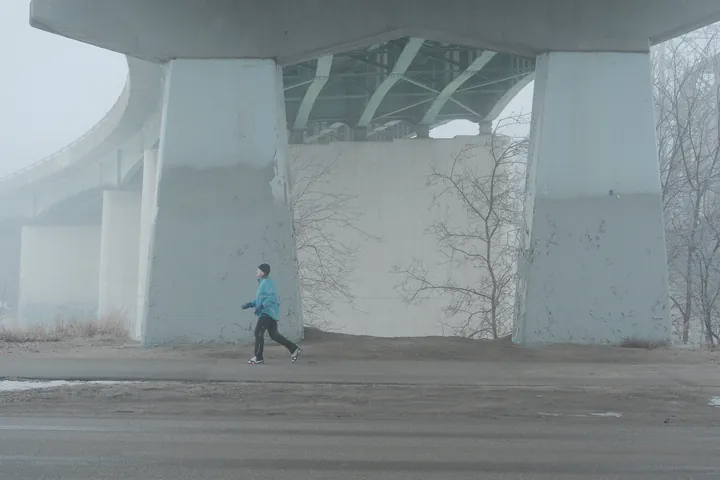 A jogger passing under a large concrete bridge on a foggy morning