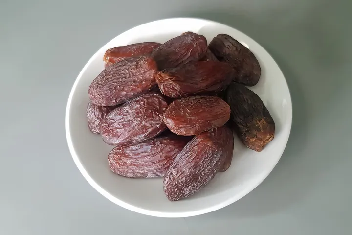 A white bowl of soft Medjool dates on a grey surface