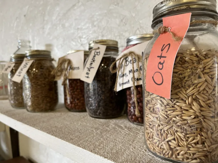Glass jars of oats, buckwheat, beans and grains with handwritten tags on a pantry shelf