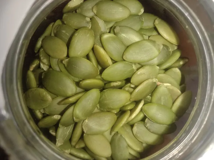Green pumpkin seeds in a glass jar, seen from above