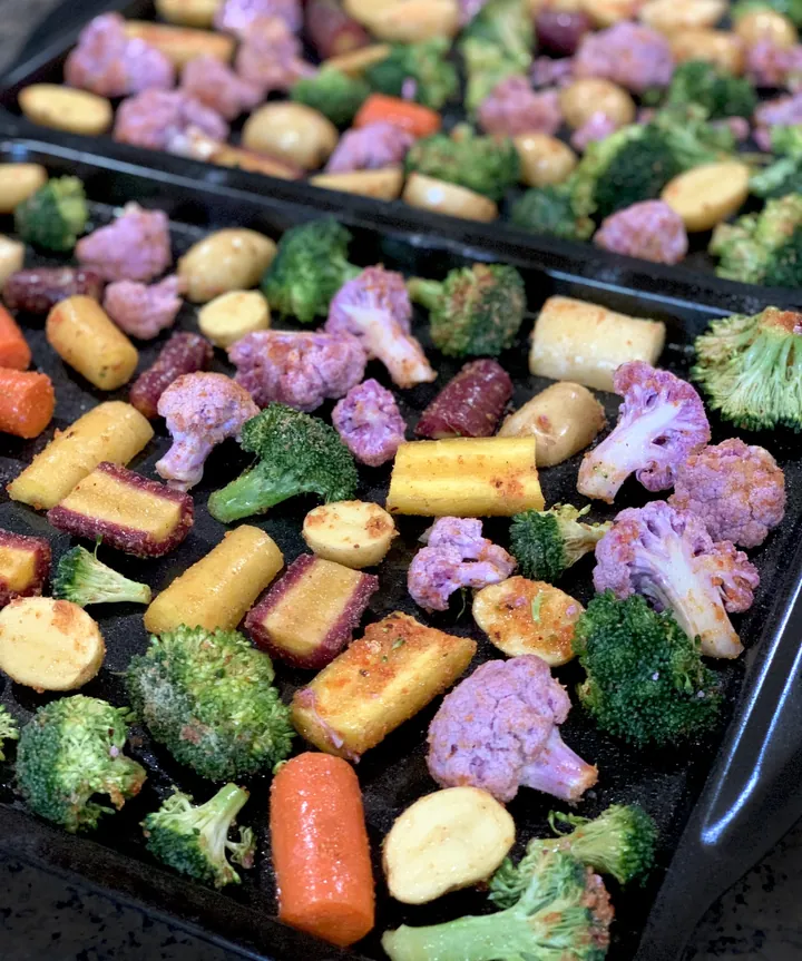 Trays of chopped broccoli, purple cauliflower, carrots and potatoes ready for roasting