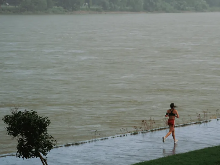 A runner splashing along a waterlogged riverside path on a grey, rainy day