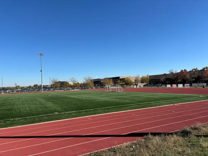 An outdoor running track curving round a playing field under a clear blue autumn sky
