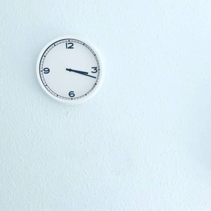 A simple white wall clock on a pale blue-white wall