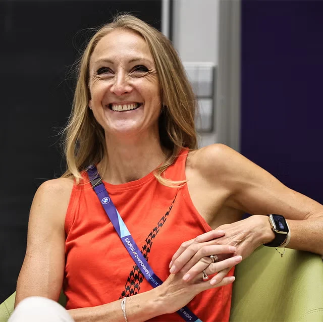 Paula Radcliffe smiling, seated in an orange vest with a European Championships lanyard